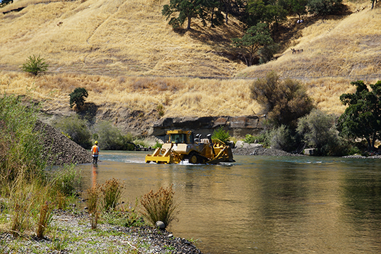 Construction equipment and crew are partially submerged while operating in a stream