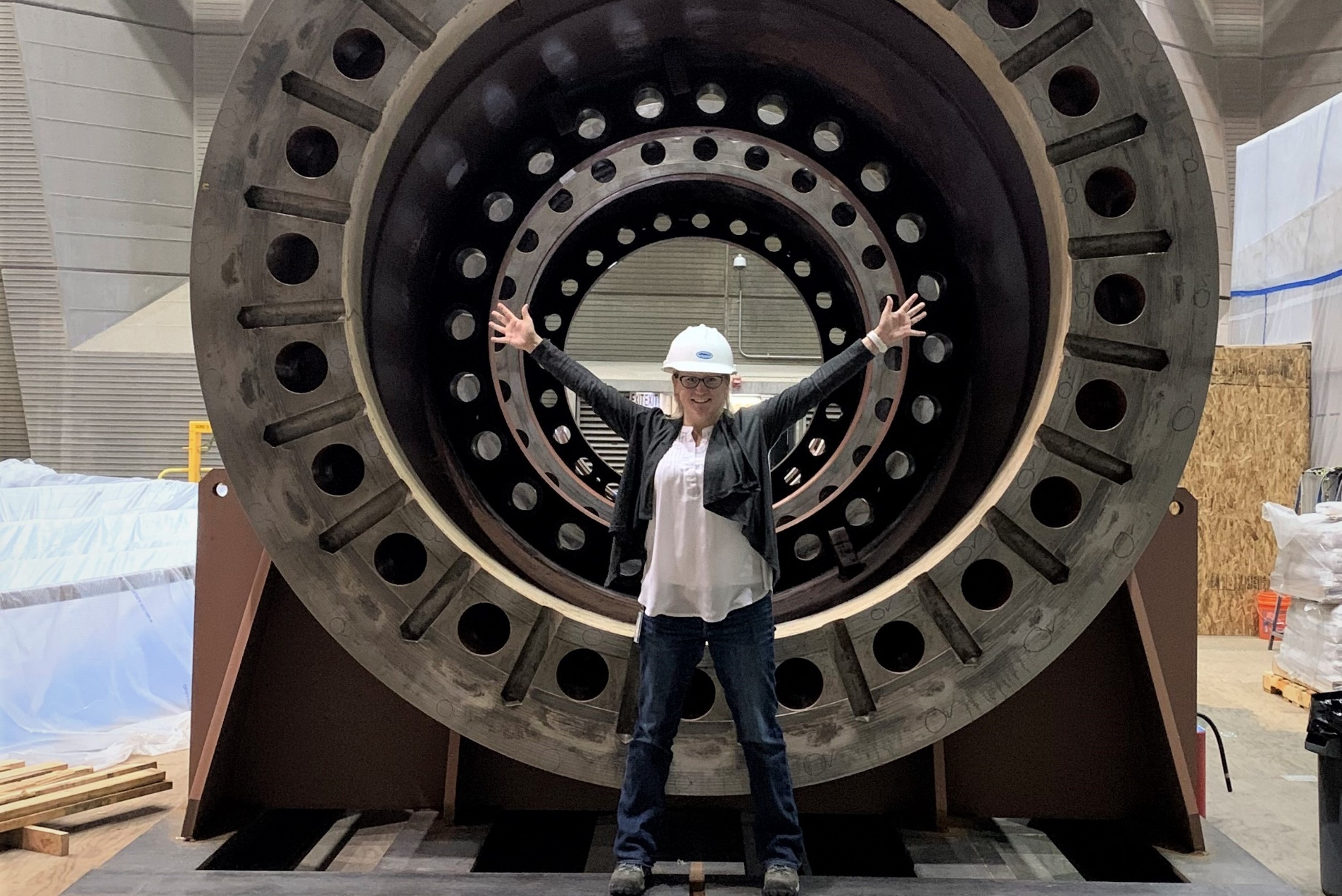 Staff Member Standing With Arms Open Wide in Front of Generator Shaft