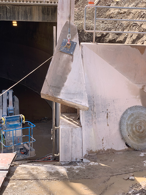 A diamond shaped piece of gray concrete is lifted by a cable from the intake structure.