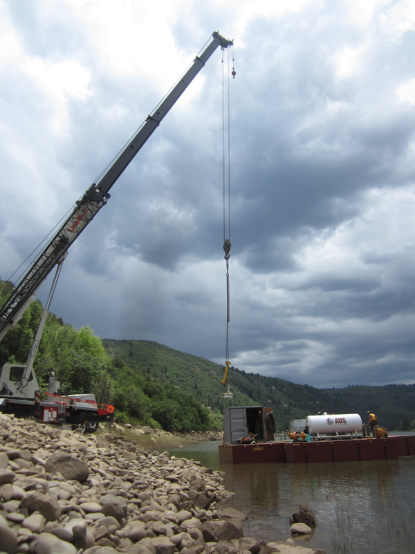 A crane on the rocky bank of Paonia Reservoir places a barge on the reservoir during a cloudy day. Photo by Matt Bryner 