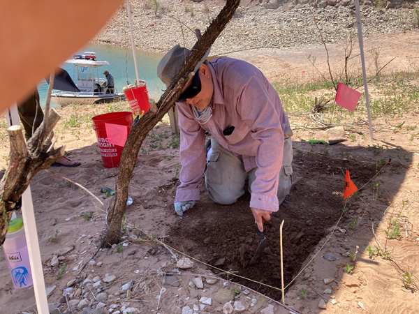 A Reclamation archaeologist is probing the ground in a small excavation site under a sunshade.