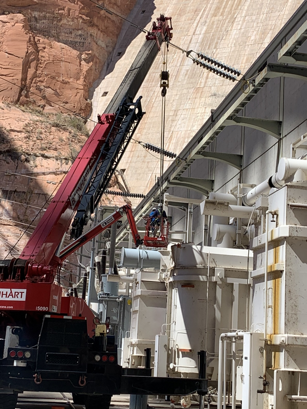 Construction workers in a man lift beginning the removal of the K7A transformer bank with a large crane in the foreground supporting the equipment. 