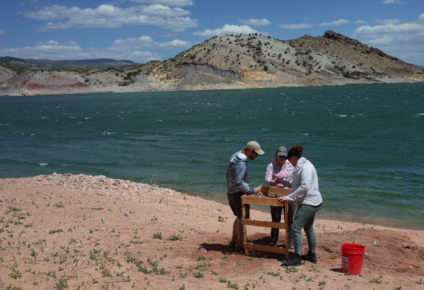 Three people gathered around a screen table on the shore of Red Fleet Reservoir near Vernal, Utah.