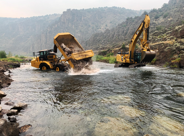Force Account operators use a dump truck and an excavator to place rocks in the riffle downriver of Linderman Diversion Dam.