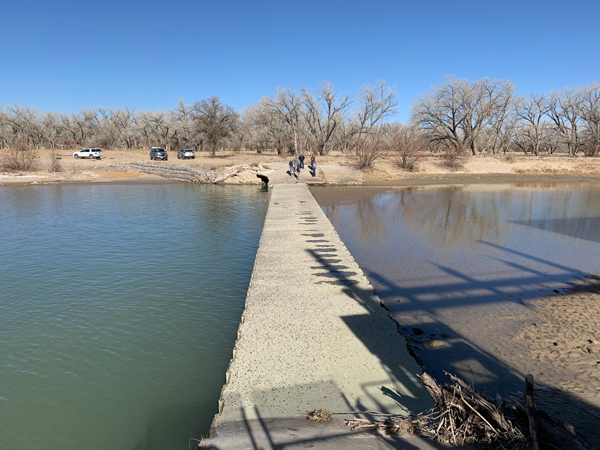 Concrete, sidewalk sized diversion dam crosses the San Juan River on a sunny, cloudless winter day.