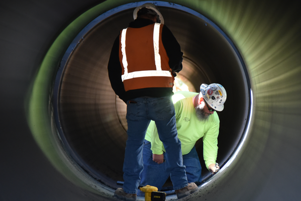 Workers on the Steinaker Service Canal Pipeline Project site trim and clean the facing surfaces on two sections of 84-inch-diameter HDPE pipe in preparation for fusing by a fusing machine.