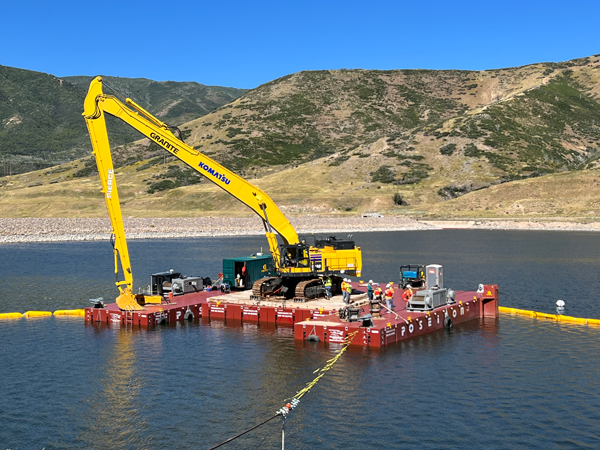 Large yellow excavatorstrapped to a working barge in Deer Creek Reservoir.